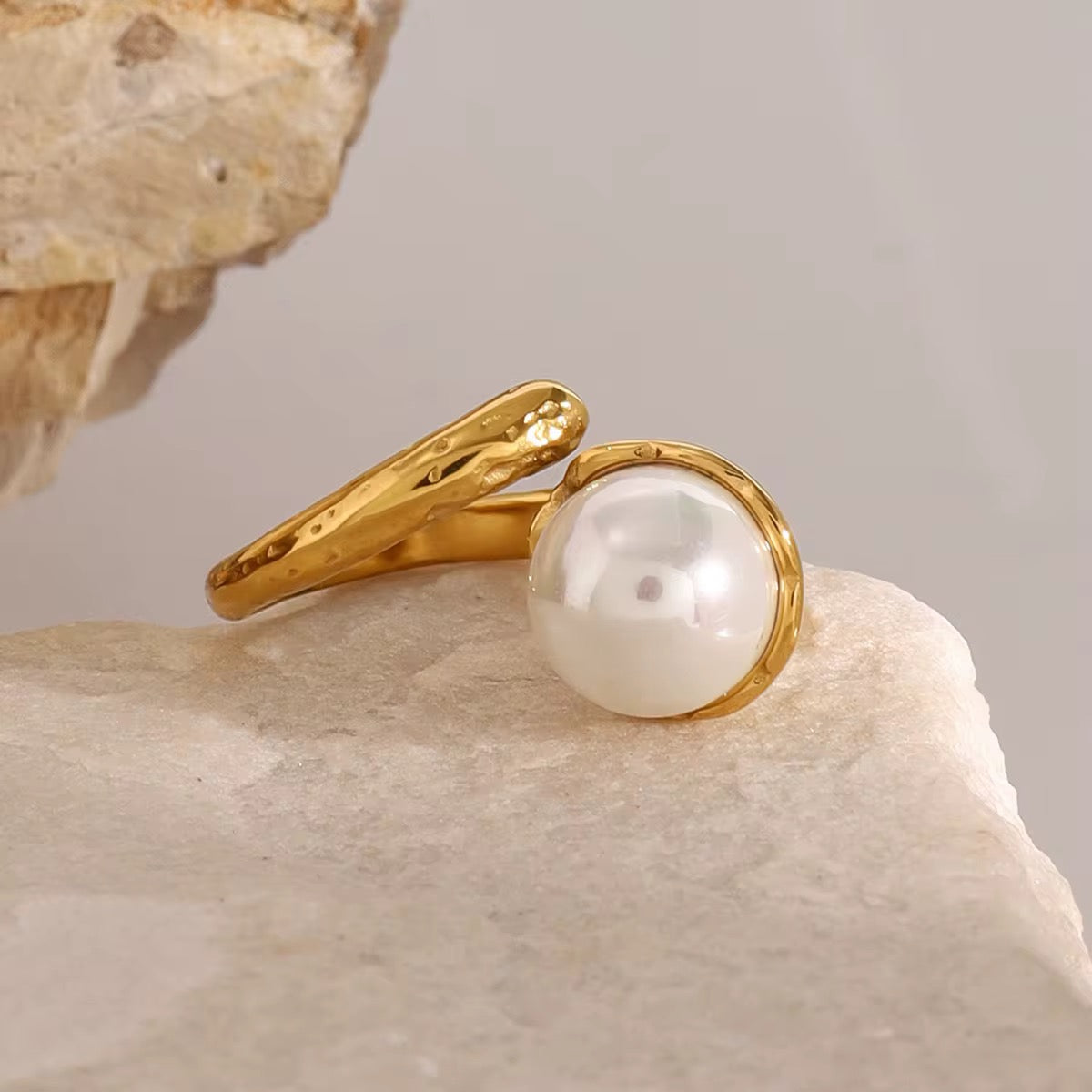 Ein vergoldeter Ring mit einem gehämmerten Perlenmuster, präsentiert auf einer strukturierten beigen Oberfläche.