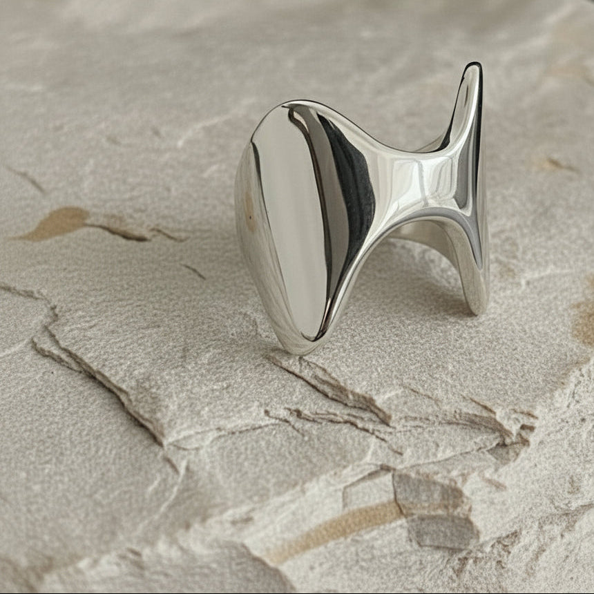 Silberner abstrakter Ring auf strukturierter weißer Oberfläche mit schwarzem Hintergrund