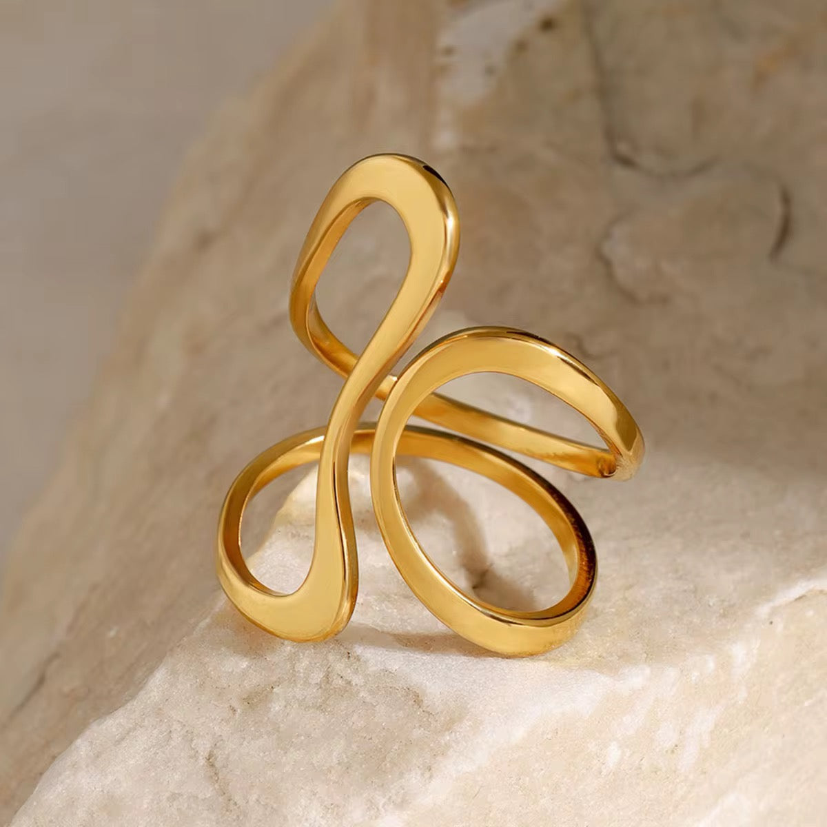 Ein vergoldeter Edelstahlring mit abstraktem Design, präsentiert auf einem Stein.