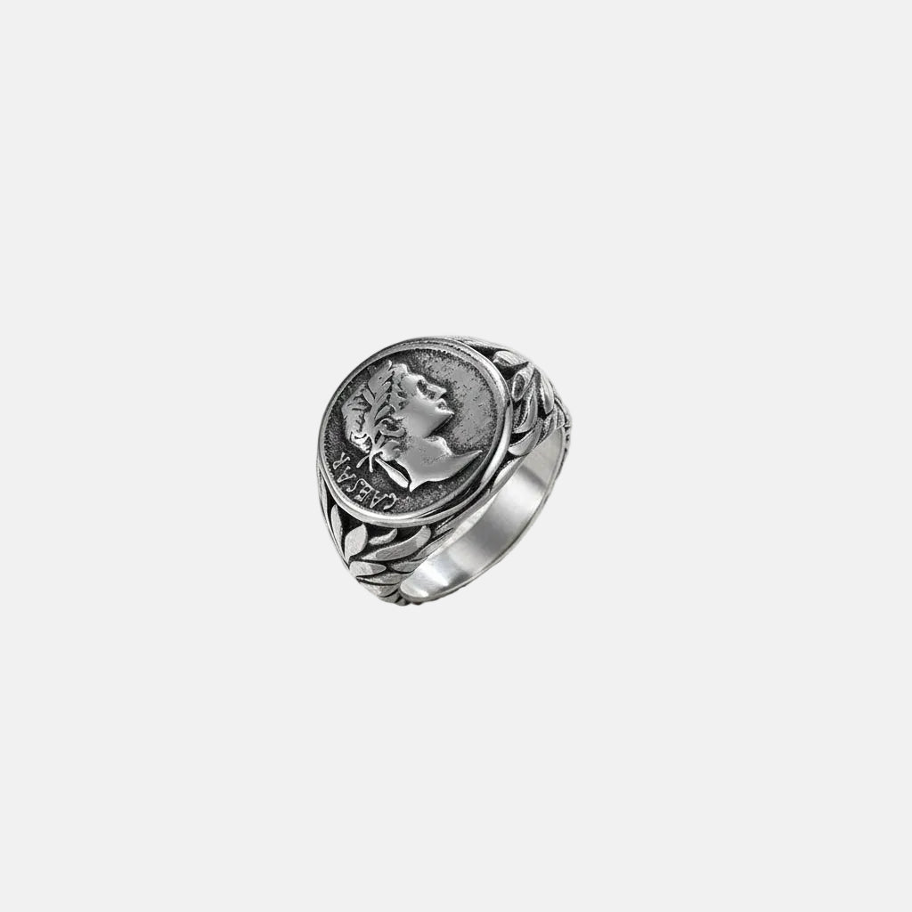 Ein versilberter Edelstahlring mit einem detaillierten Design und einer geprägten Caesar-Münze als Mittelstück, präsentiert auf weißem Untergrund.