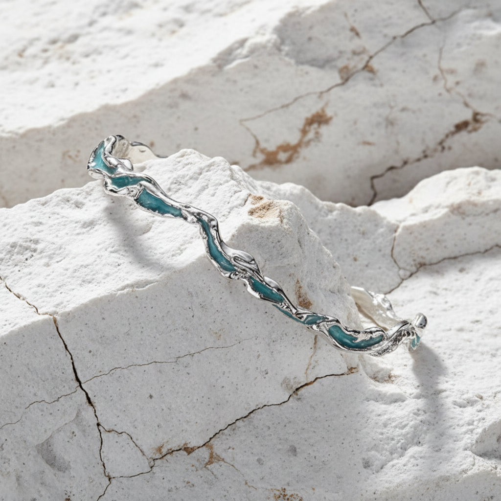 Ein Armband aus Sterlingsilber mit mintblauer Tönung, präsentiert auf einer dunklen, strukturierten Oberfläche.