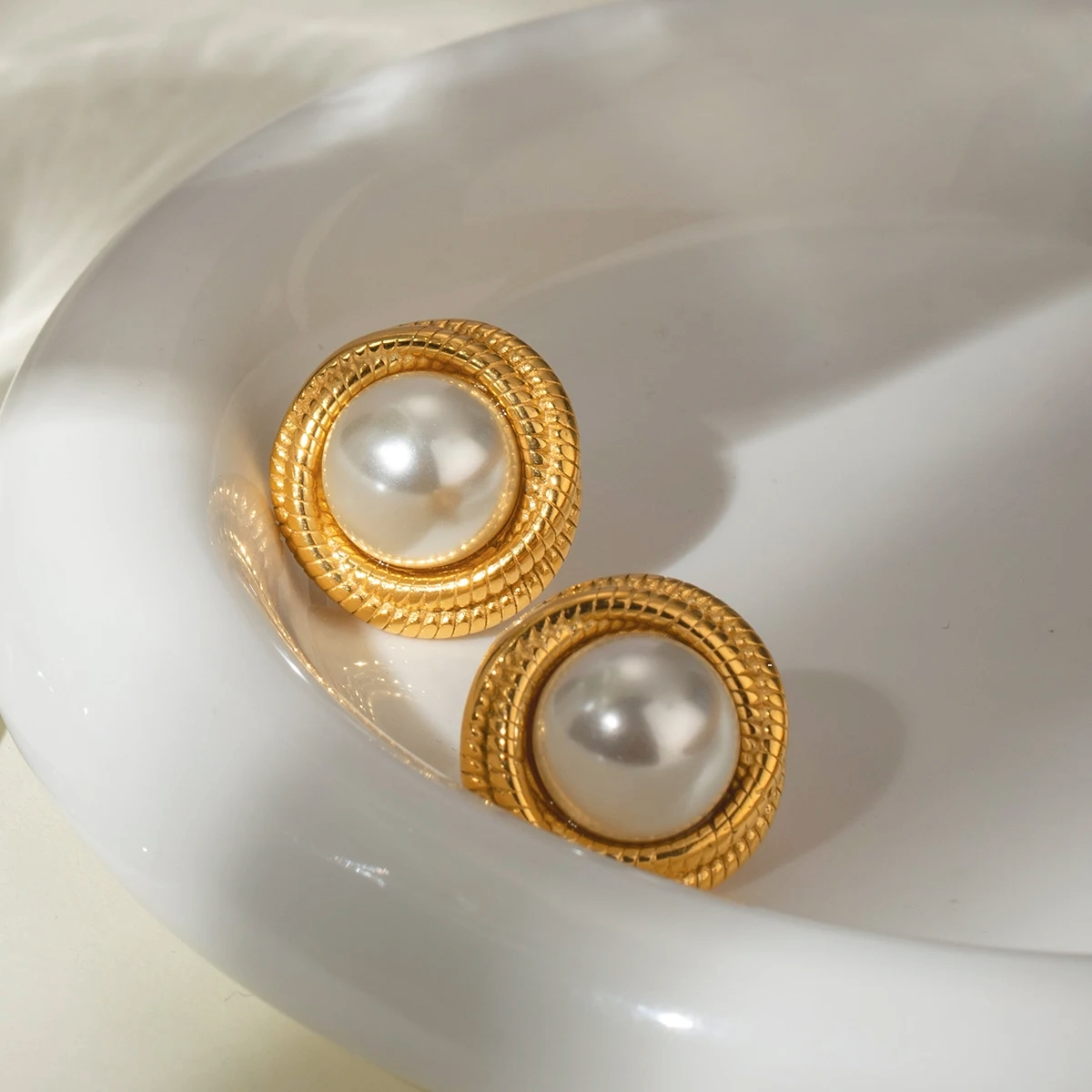 Gold-framed pearl earrings on a white surface