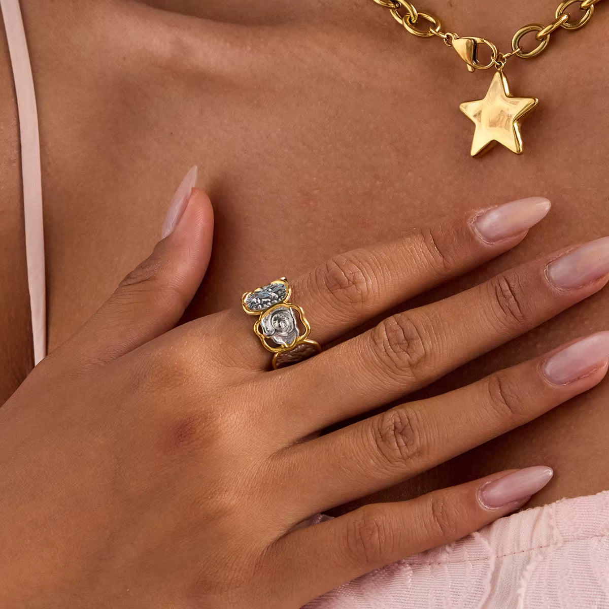 Hand wearing a gold ring with gemstones, gold necklace with star pendant on a brown background