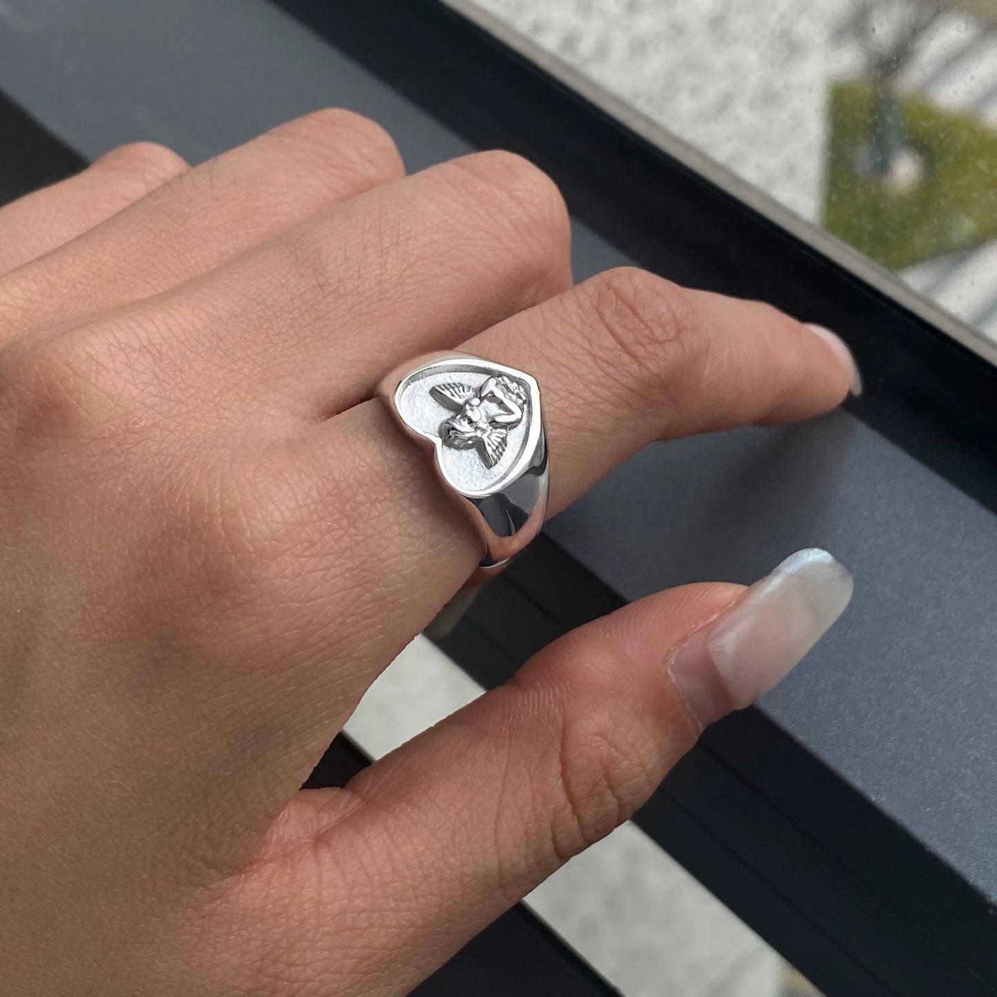 Hand wearing a silver ring with a detailed design, blurred background