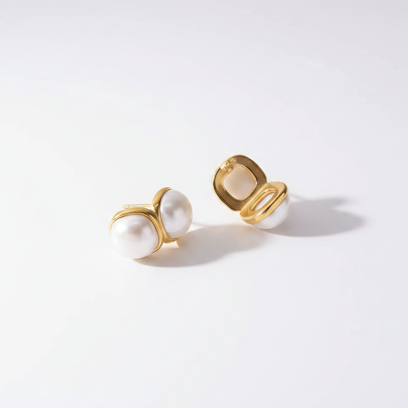 Pair of gold and pearl earrings on a light gray background