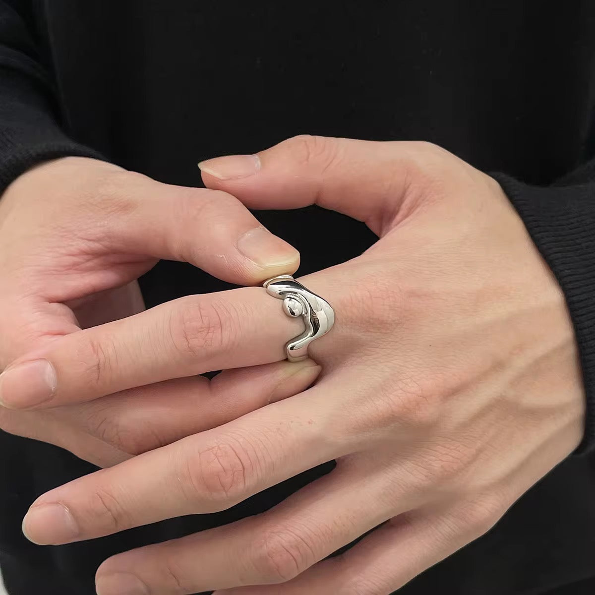 Close-up of hands with a silver ring on a black background