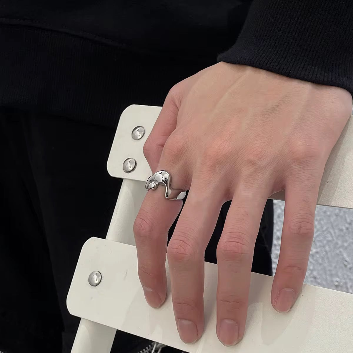 Hand wearing a silver ring on a white chair with a black background