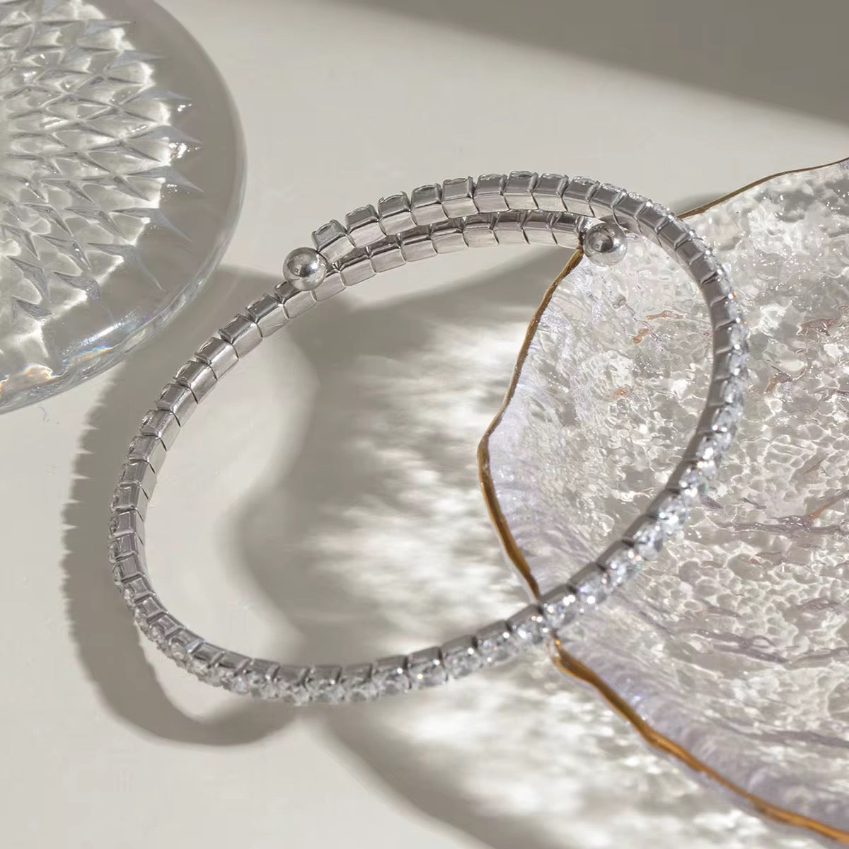 Ein flexibles Edelstahlarmband mit Goldbeschichtung und Zirkoniasteinen, präsentiert auf einer weißen Fläche mit reflektierender Lichtquelle.