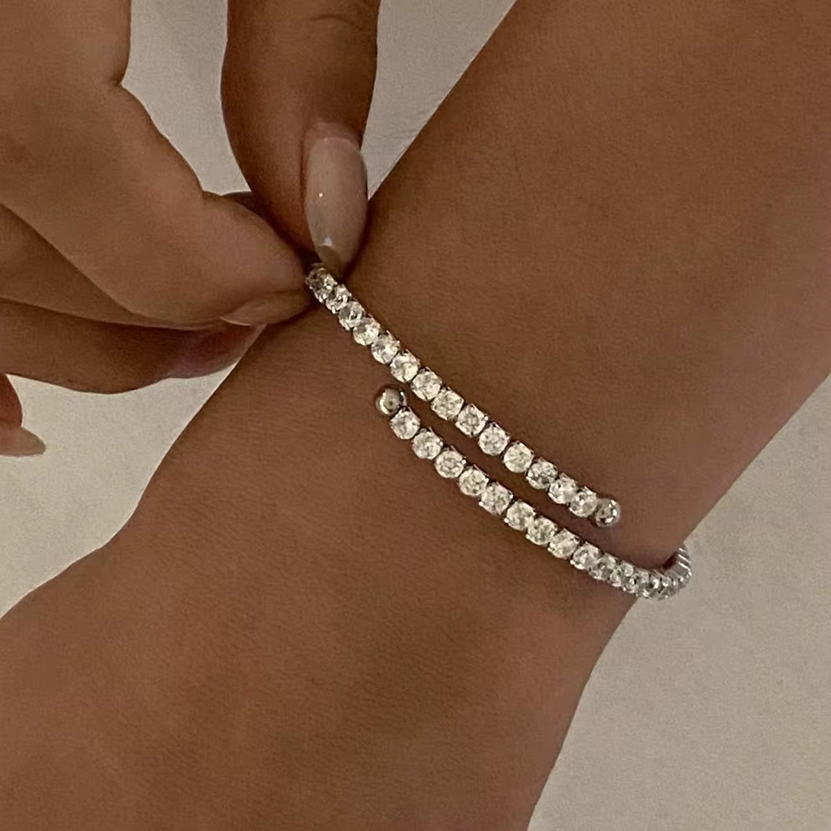 Ein flexibles Edelstahlarmband mit Goldbeschichtung und Zirkoniasteinen, präsentiert auf einer weißen Fläche mit reflektierender Lichtquelle.