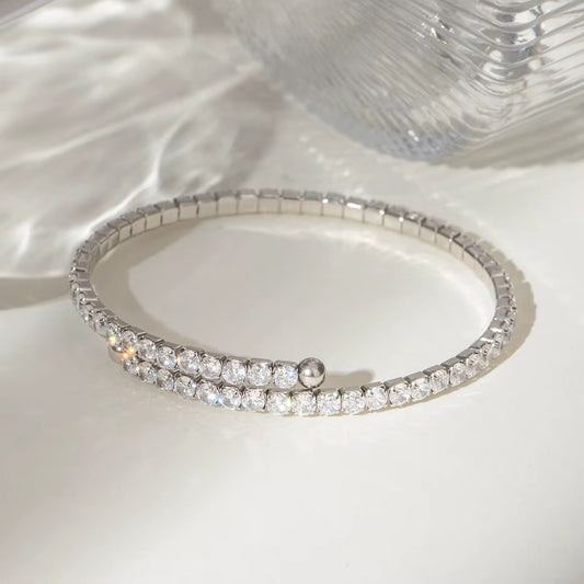 Ein flexibles Edelstahlarmband mit Goldbeschichtung und Zirkoniasteinen, präsentiert auf einer weißen Fläche mit reflektierender Lichtquelle.