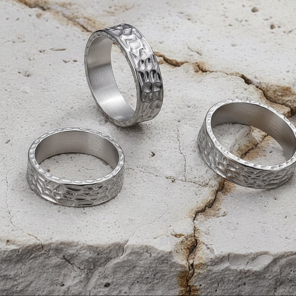 Zwei Edelstahlringe mit strukturiertem Muster, platziert auf einer dunklen, strukturierten Oberflaeche.