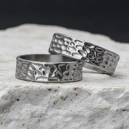 Zwei Edelstahlringe mit strukturiertem Muster, platziert auf einer dunklen, strukturierten Oberflaeche.