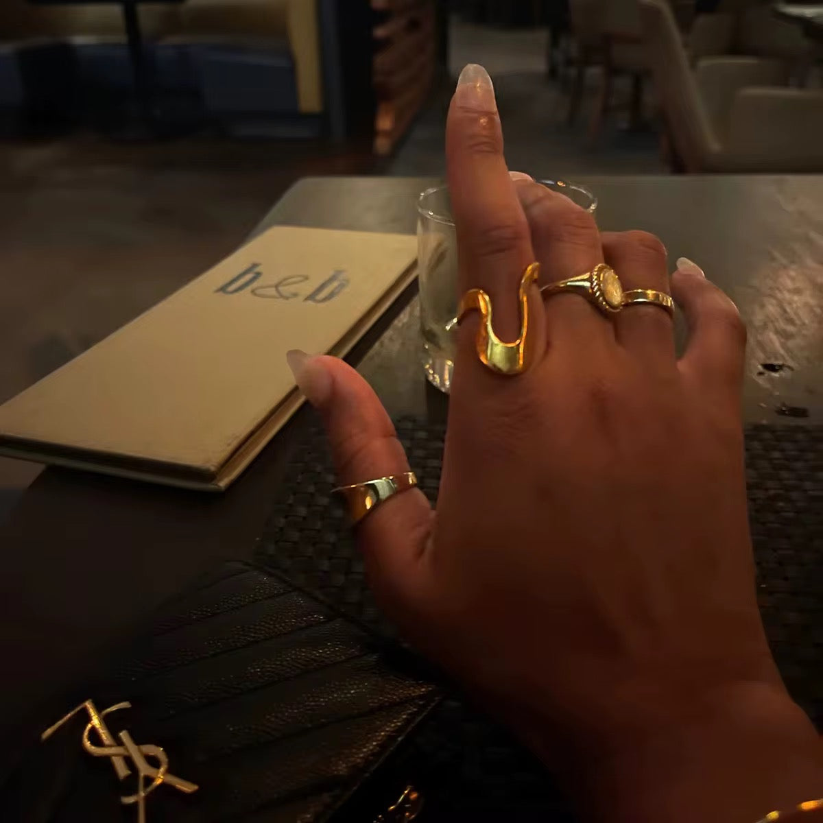 Die Hand einer Frau, an deren Finger ein vergoldeter Edelstahlring mit einer unregelmäßigen, geschwungenen Form zu sehen ist.