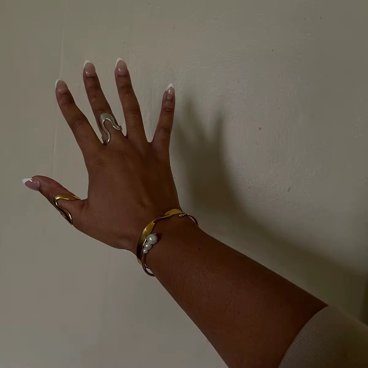 Die Hand einer Frau, an deren Finger ein vergoldeter Edelstahlring mit einer unregelmäßigen, geschwungenen Form zu sehen ist.