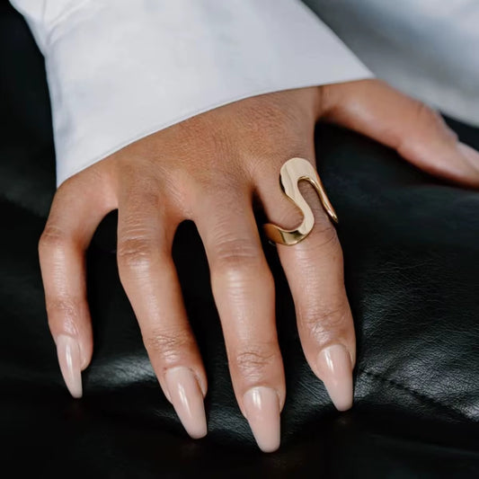 Die Hand einer Frau, an deren Finger ein vergoldeter Edelstahlring mit einer unregelmäßigen, geschwungenen Form zu sehen ist.
