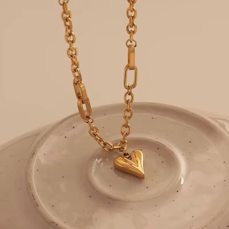 Goldfarbener herzförmiger Anhänger an einer Goldkette vor beigem Hintergrund
