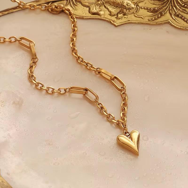 Goldkettenarmband mit Herzanhänger auf strukturierter beiger Oberfläche