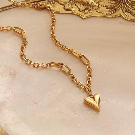 Goldkettenarmband mit Herzanhänger auf strukturierter beiger Oberfläche