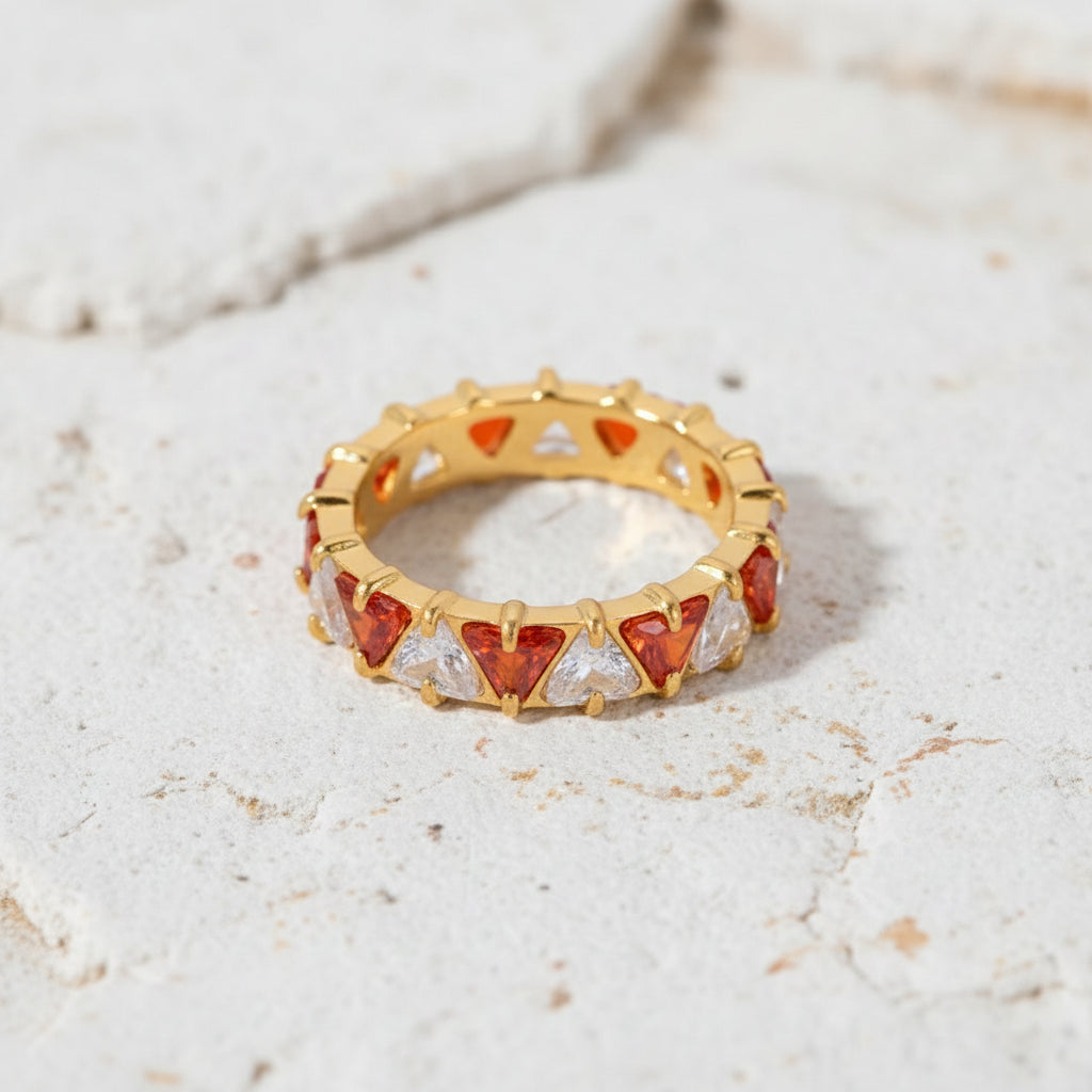 Goldring mit roten und klaren Edelsteinen auf einer grünen Marmoroberfläche