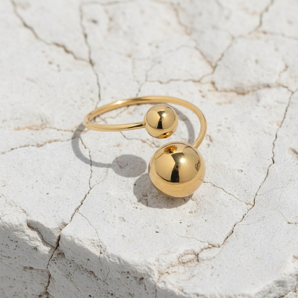 Goldring mit zwei kugelförmigen Perlen auf hellblauem Marmorhintergrund