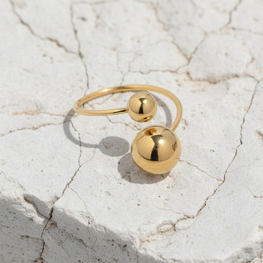 Goldring mit zwei kugelförmigen Perlen auf hellblauem Marmorhintergrund