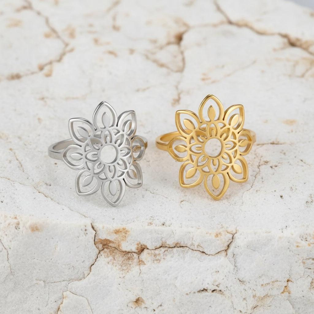 Zwei Ringe, einer mit Silberbeschichtung und der andere mit Goldbeschichtung, mit einem filigranen Sonnenblumenmotiv, auf einer rosa Stoffoberfläche platziert.