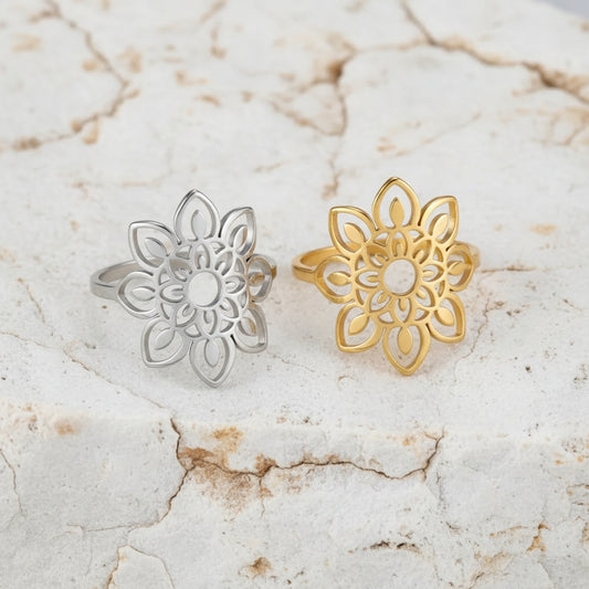 Zwei Ringe, einer mit Silberbeschichtung und der andere mit Goldbeschichtung, mit einem filigranen Sonnenblumenmotiv, auf einer rosa Stoffoberfläche platziert.