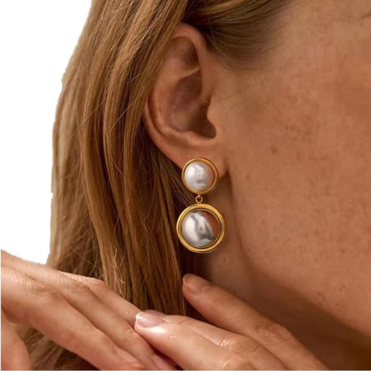 Eine Frau, die vergoldete Edelstahl- Ohrringe mit Perlenverzierung trägt.