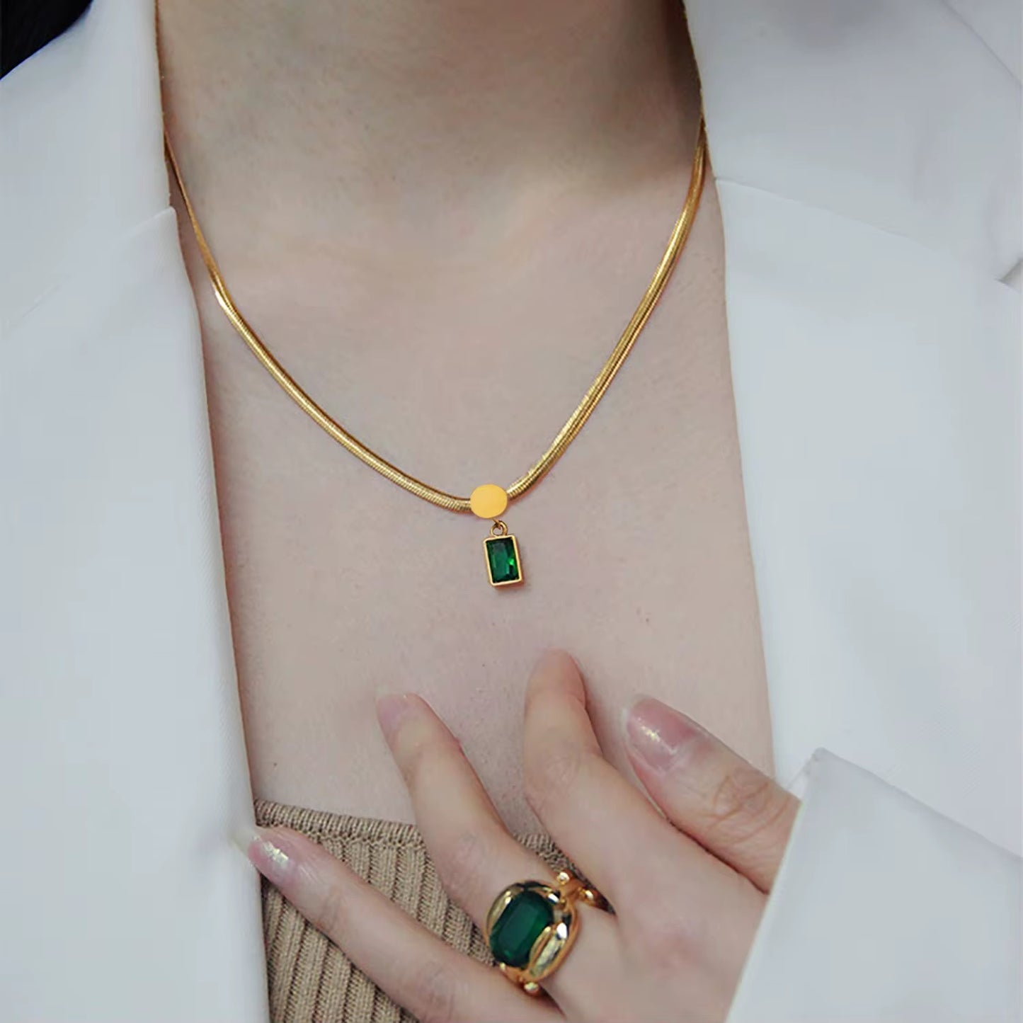 Eine Frau, die eine vergoldete Edelstahl-Schlangenkette mit einem Anhänger mit einem grünen Zirkonstein trägt.