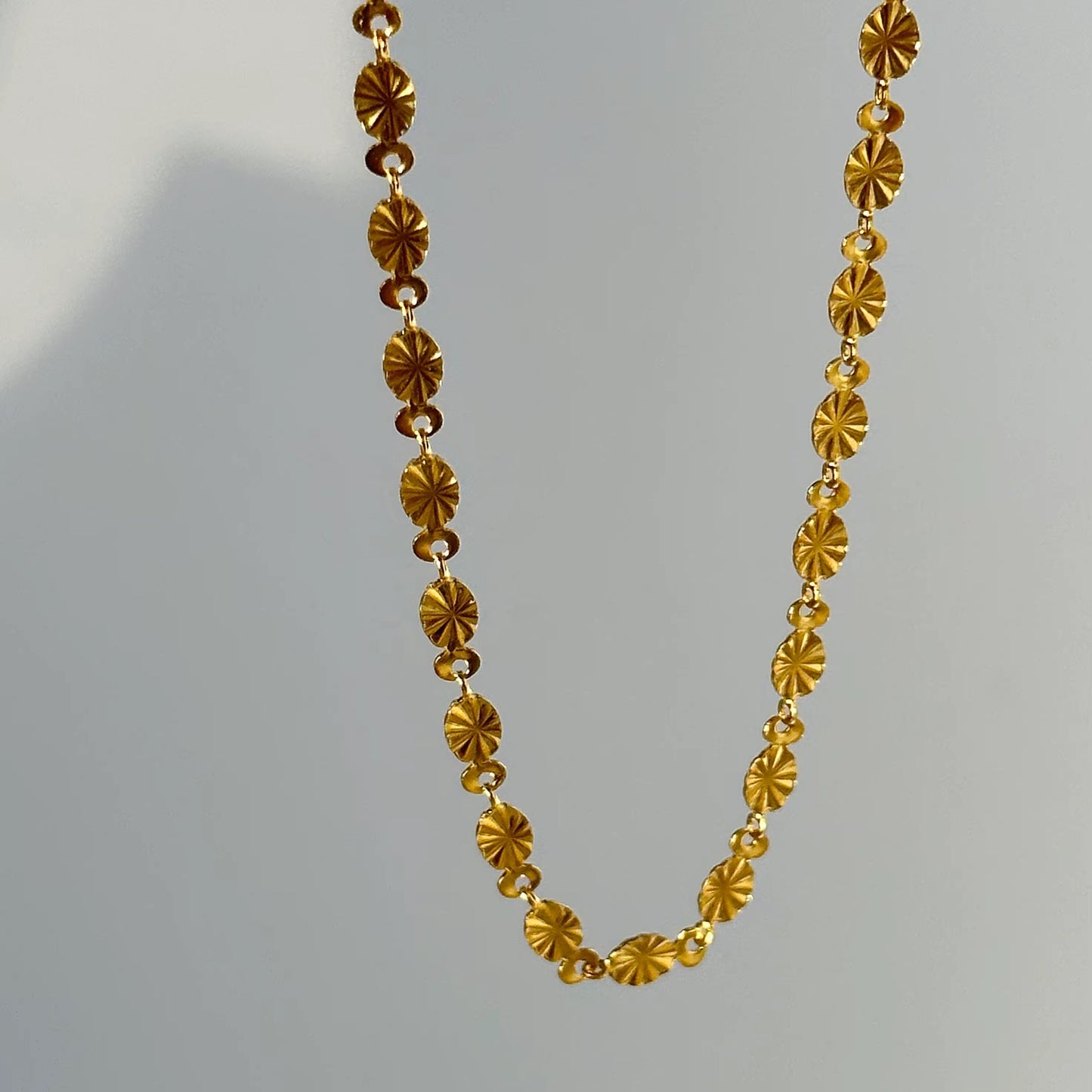 Nahaufnahme einer Frau, die eine vergoldete Edelstahlkette mit geprägten Palastmotiven trägt.