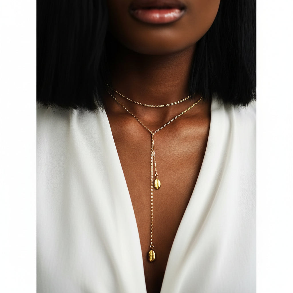 Eine Frau, die eine vergoldete Edelstahlkette mit einem Muschelanhänger trägt. Die Kette ist mehrreihig, wobei sich der Hauptanhänger in der Mitte der Brust befindet und von kleineren Anhängern begleitet wird, die nach unten hängen.