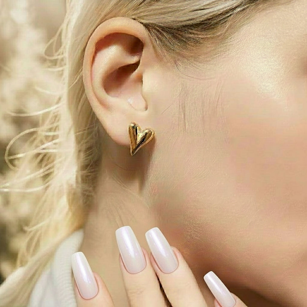 Gold heart-shaped earring worn by a person with blonde hair.