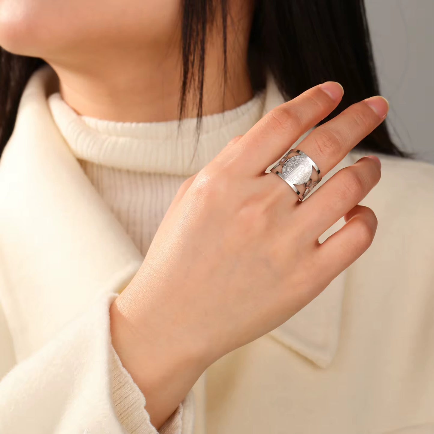 Eine Person, die einen weißen Pullover trägt und einen vergoldeten Edelstahlring am Finger trägt.