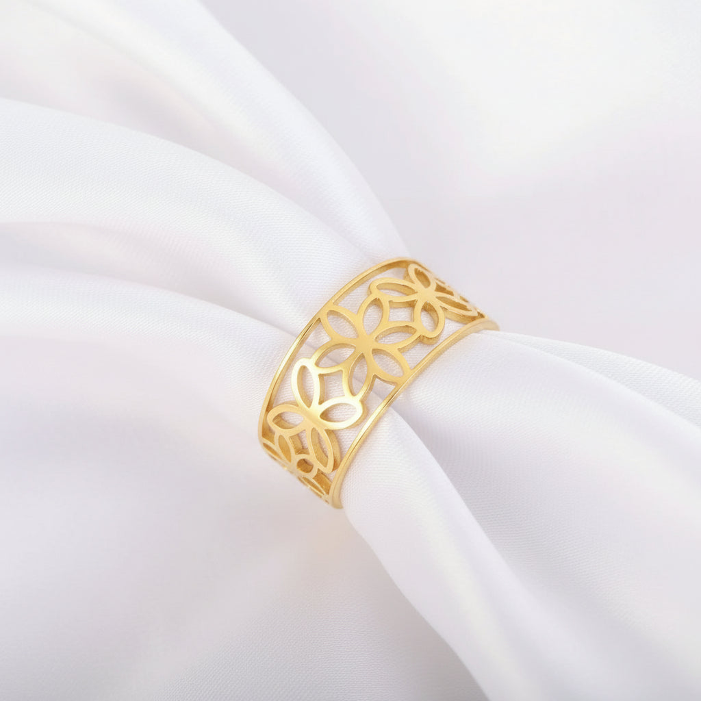 Ein Ring aus 18 Karat vergoldetem Edelstahl mit einem hohlen Blumenmotiv, präsentiert auf einem Satinstoff.