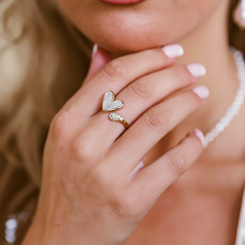 Die Hand einer Frau, die einen vergoldeten Edelstahlring mit einem Muschelherz-Design und Strassstein-Verzierungen am Finger präsentiert.