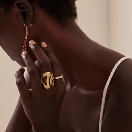 Eine Person, die einen vergoldeten Edelstahlring mit einem Wellenmuster am Finger trägt.