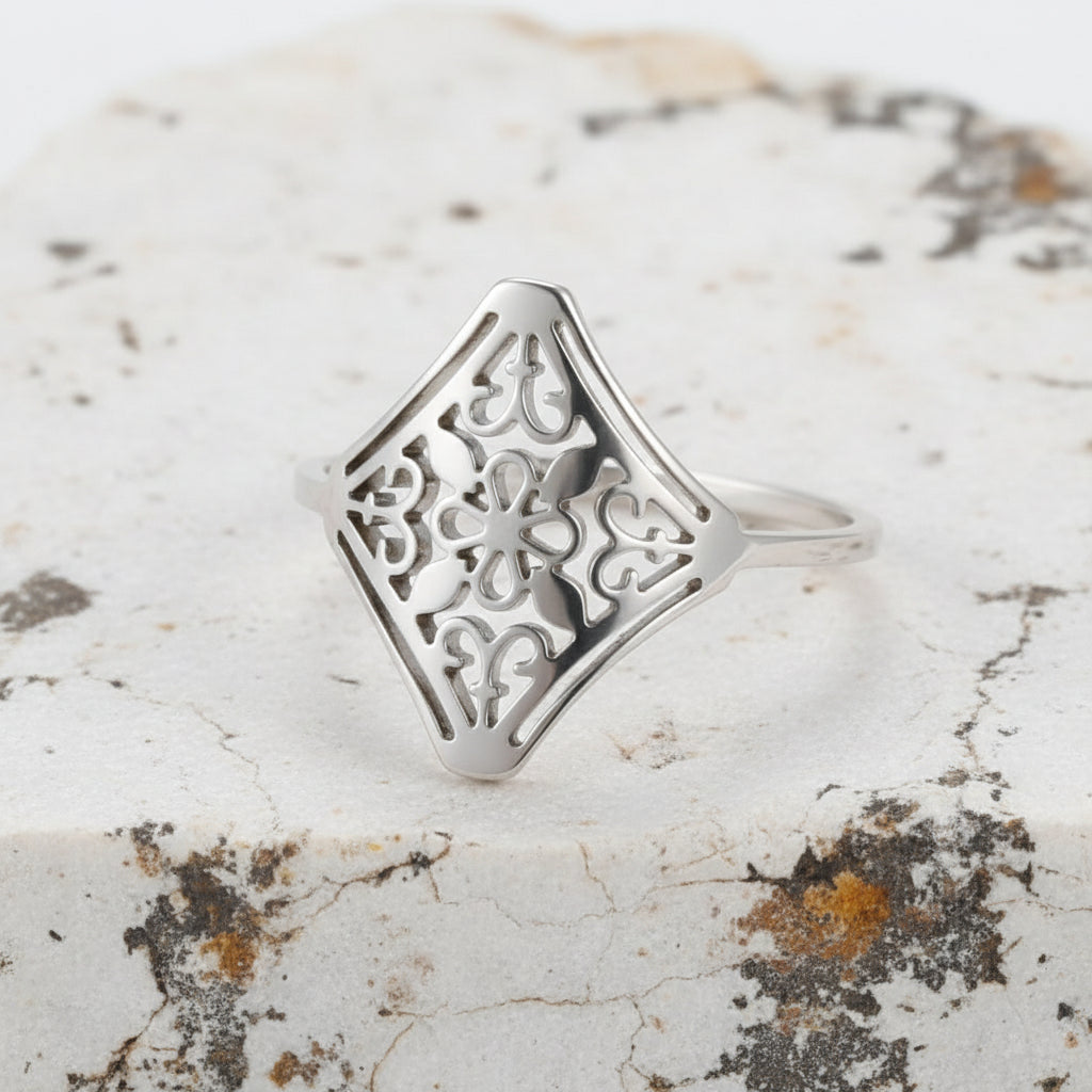 Ein vergoldeter Edelstahlring mit einem Vintage-Blumenmuster, präsentiert auf beigem Hintergrund.