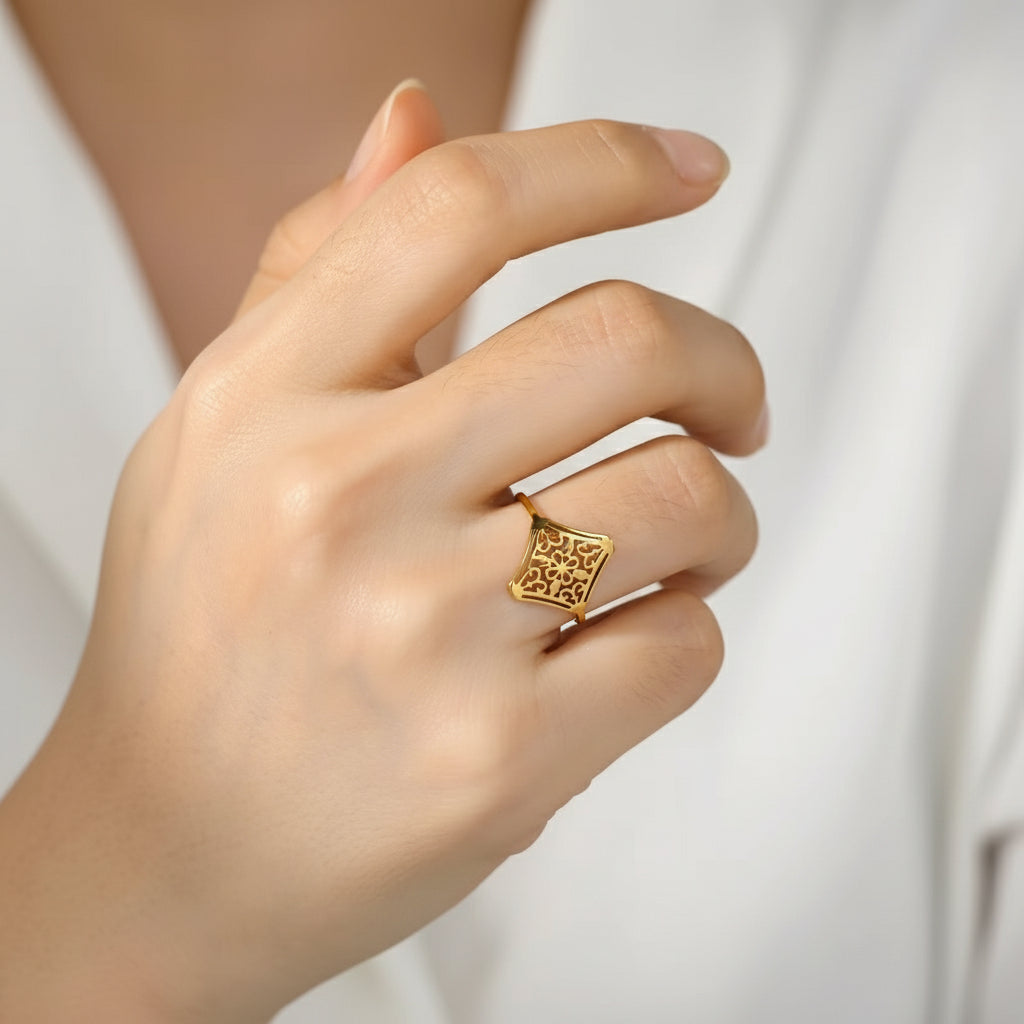 Ein vergoldeter Edelstahlring mit einem Vintage-Blumenmuster, präsentiert auf beigem Hintergrund.