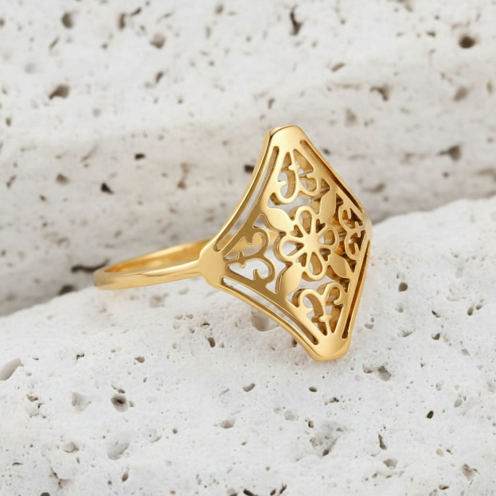 Ein vergoldeter Edelstahlring mit einem Vintage-Blumenmuster, präsentiert auf beigem Hintergrund.