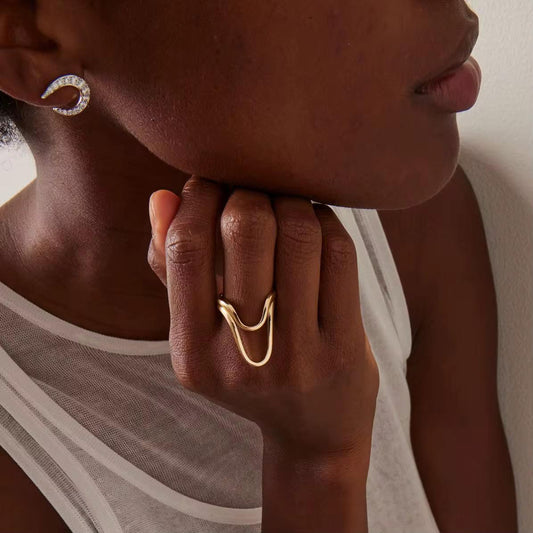 Nahaufnahme einer Person, die goldene Creolen und Ringe trägt, vor einem neutralen Hintergrund