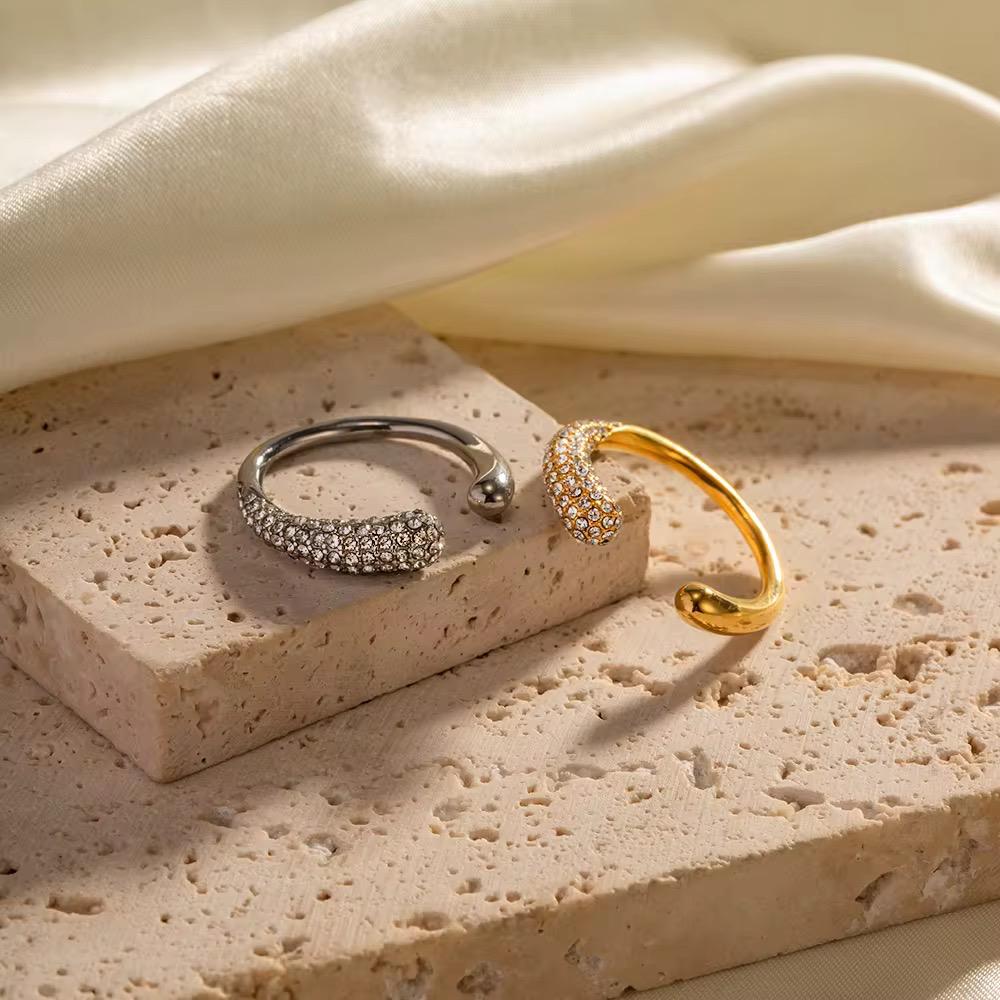 Two rings, one silver and one gold, on a textured stone surface with a soft fabric background.
