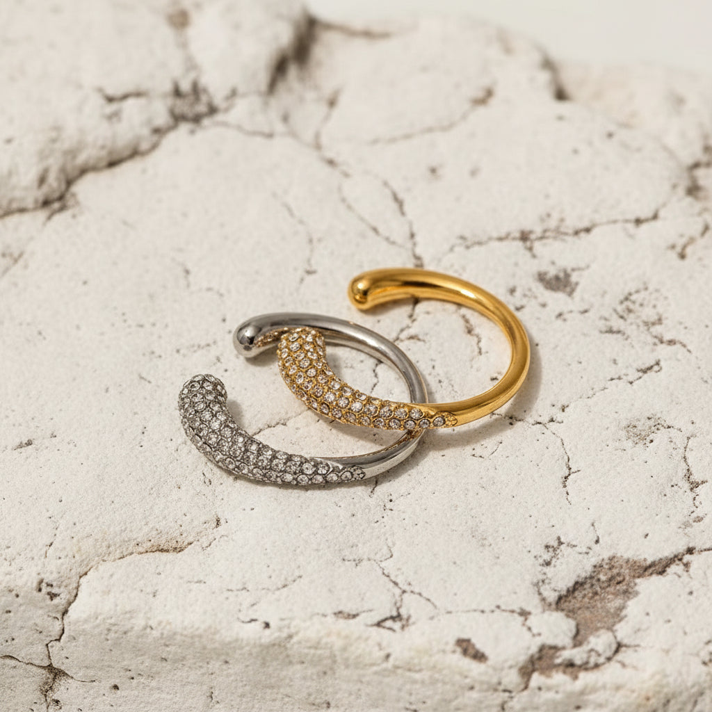 Ein vergoldeter Edelstahlring mit einem Design aus Weiß- und Gelbgold, verziert mit einem natürlichen Edelstein, präsentiert auf einer satinierten Oberfläche.