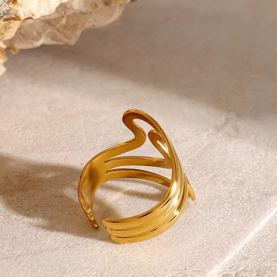 Goldring mit wellenförmigem Design auf beiger Steinoberfläche