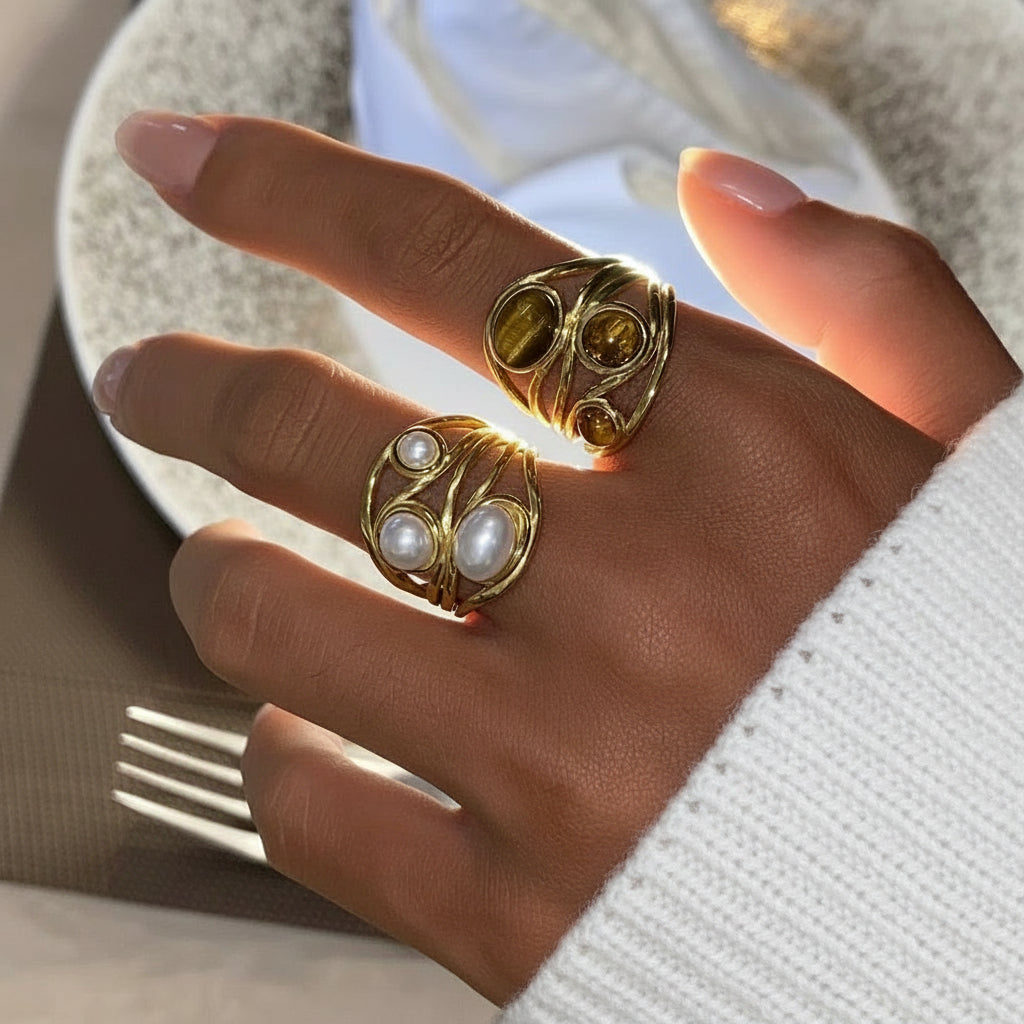 Hand mit zwei Goldringen mit Edelsteinen und Perlen auf neutralem Hintergrund