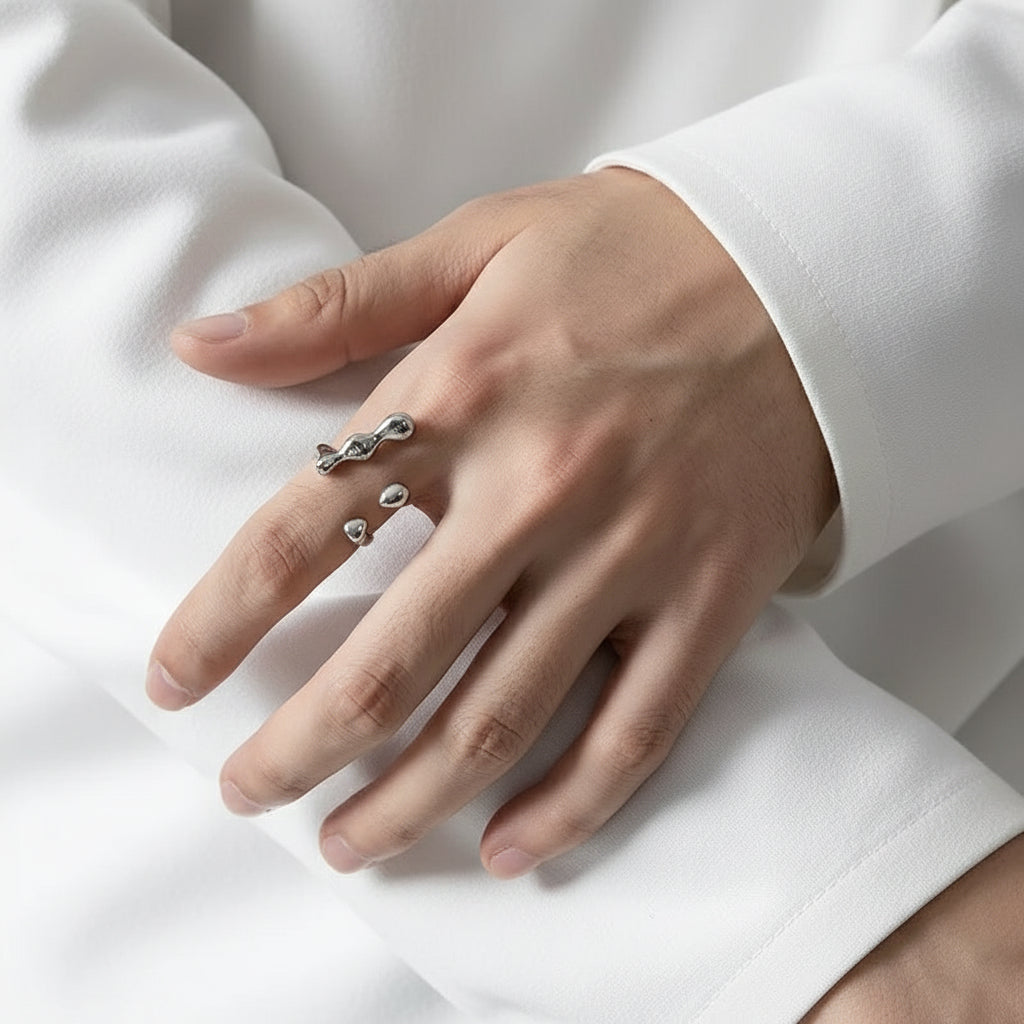 Eine Person, die einen versilberten Edelstahlring mit einem flüssigkeitsähnlichen Design am Finger trägt.