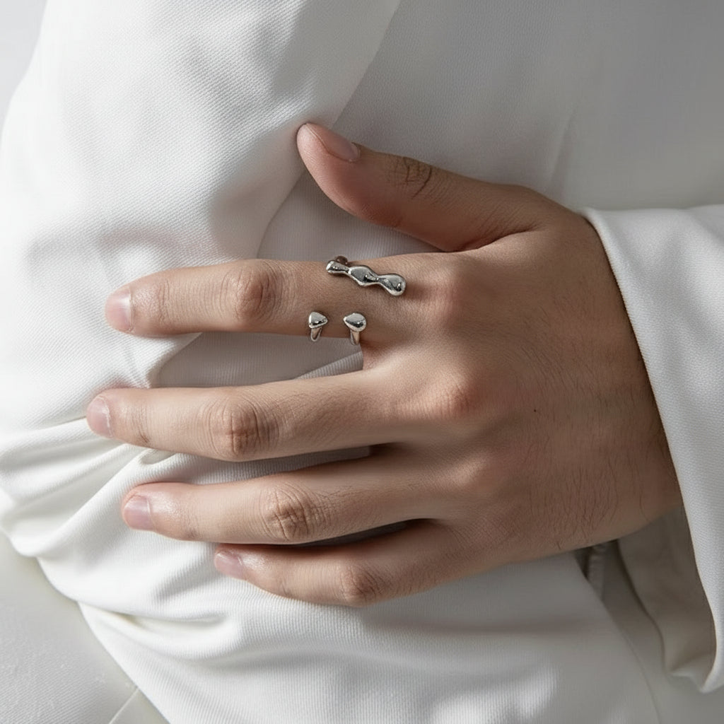 Eine Person, die einen versilberten Edelstahlring mit einem flüssigkeitsähnlichen Design am Finger trägt.