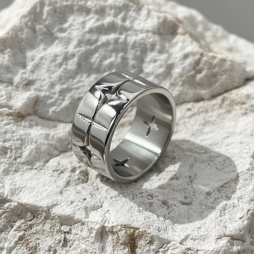 Ein versilberter Edelstahlring mit einem Sternmuster auf strukturiertem Hintergrund.