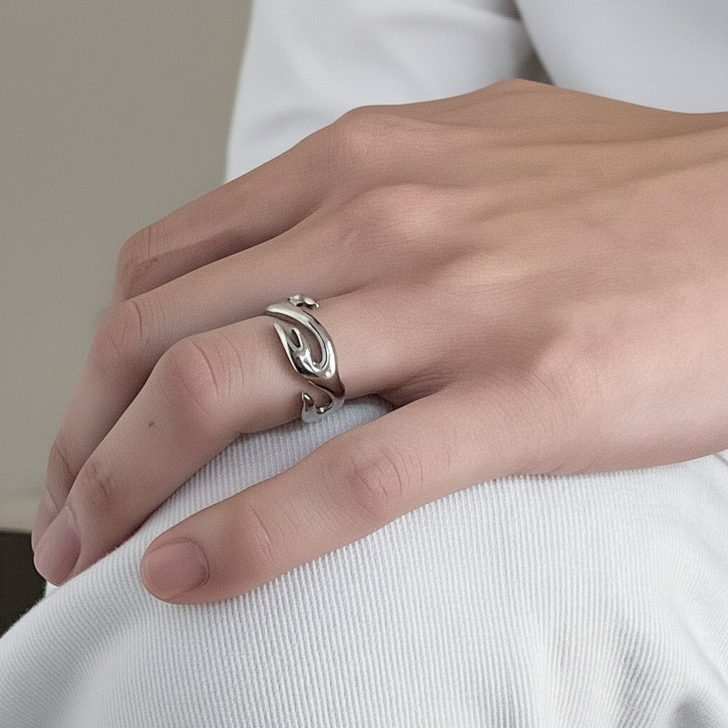 Ein versilberter Edelstahlring mit Flammenmotiv, präsentiert auf einer dunklen strukturierten Oberfläche.