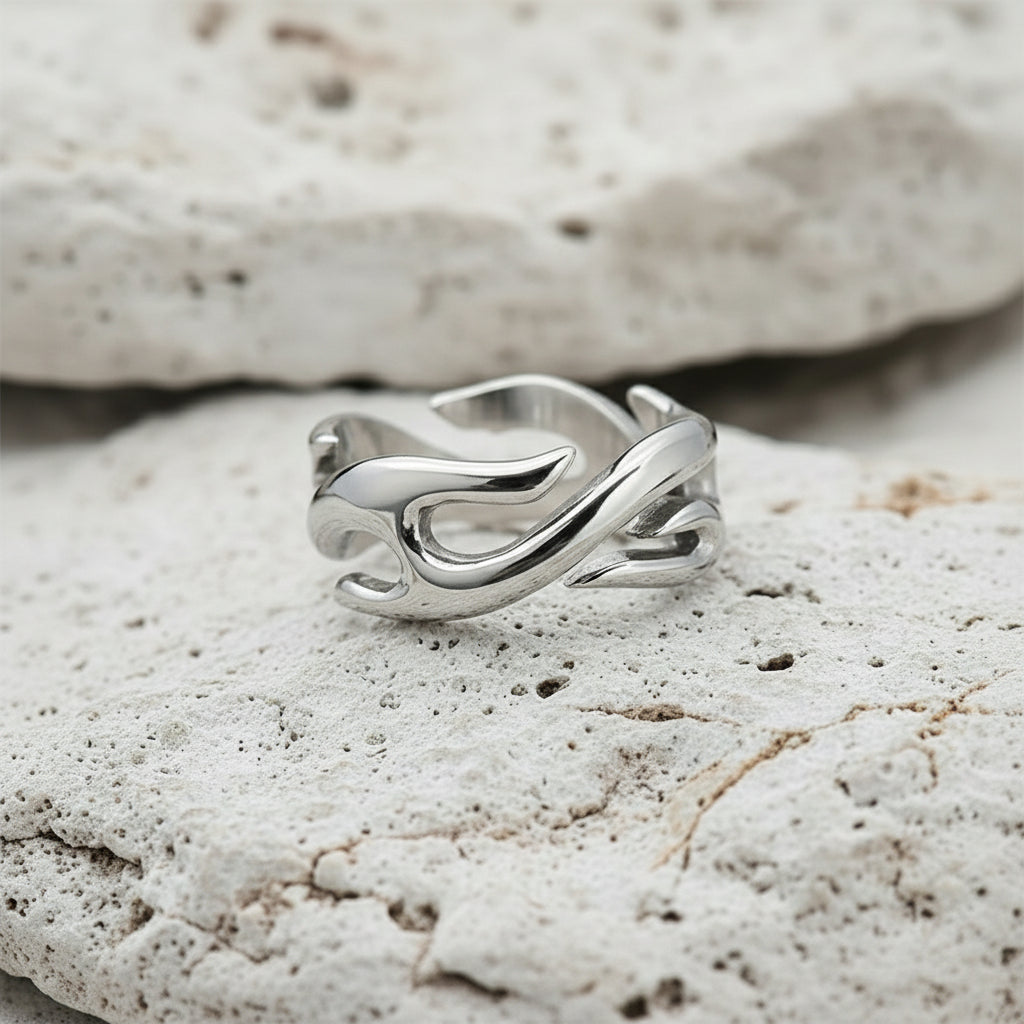 Ein versilberter Edelstahlring mit Flammenmotiv, präsentiert auf einer weissen strukturierten Oberfläche.