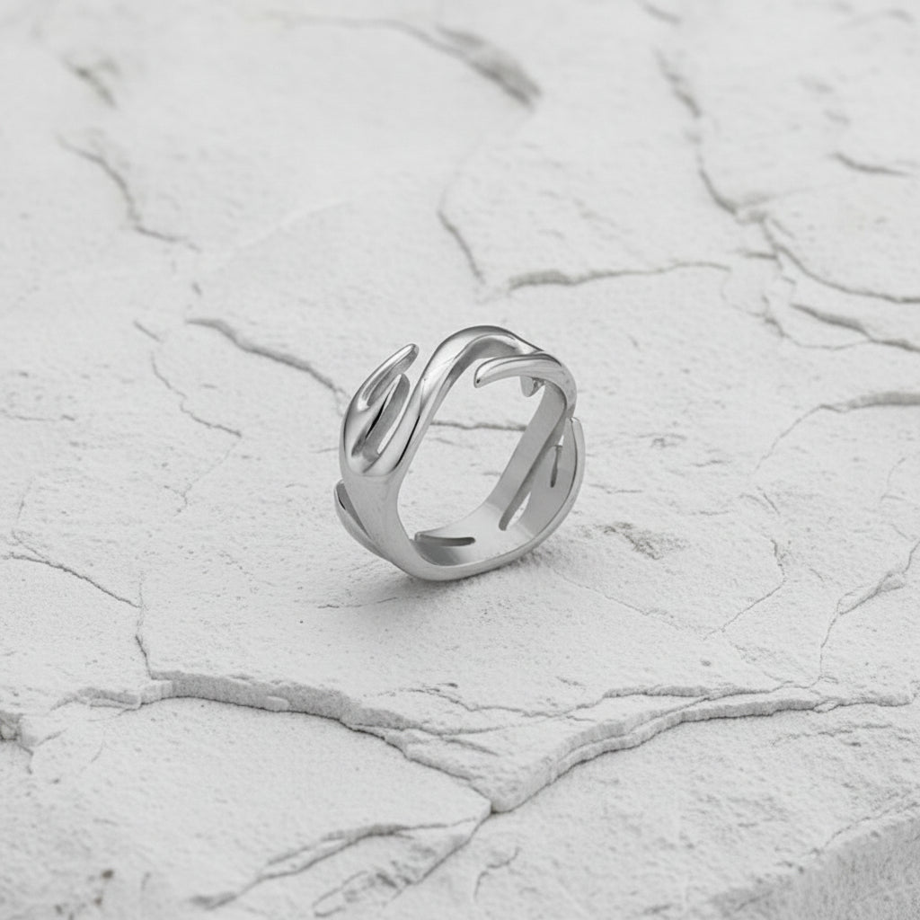 Ein versilberter Edelstahlring mit Flammenmotiv, präsentiert auf einer dunklen strukturierten Oberfläche.